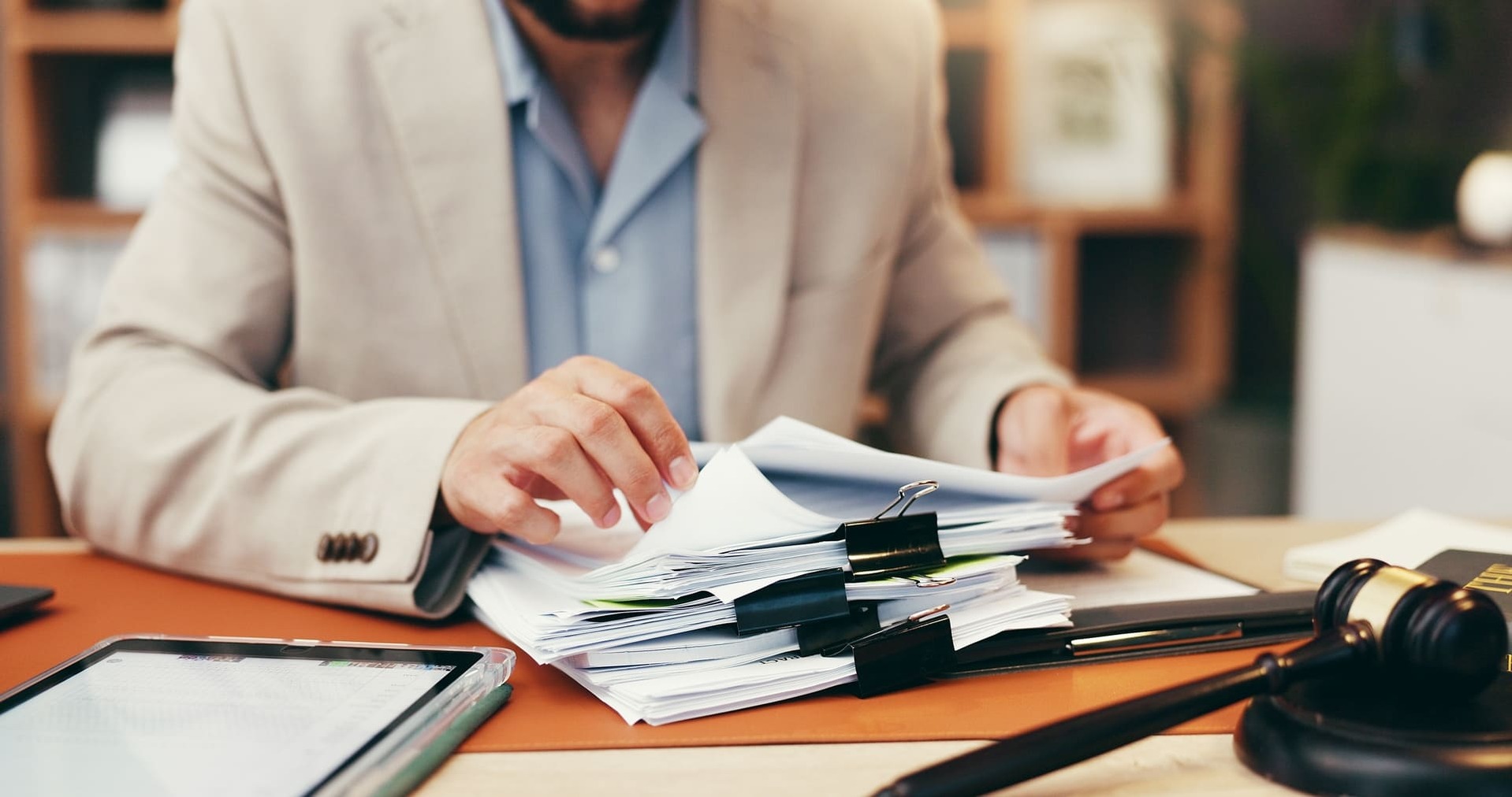 Hombre organizando una pila de expedientes en papel en un escritorio con un mazo de juez y tableta. La imagen simboliza la actividad procedimental y regulatoria que define qué es el Derecho Administrativo.