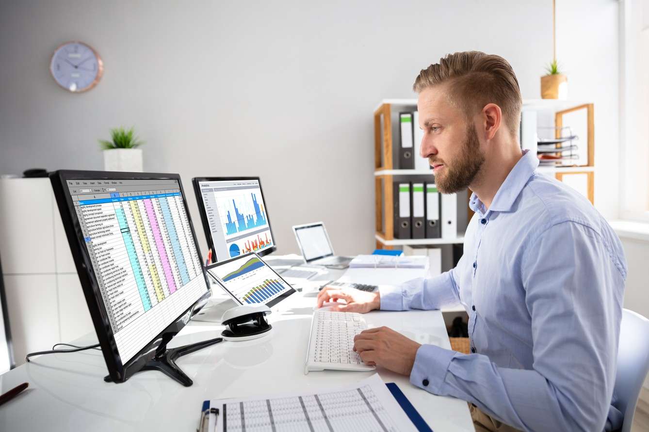 Profesional trabajando en oficina con hojas de cálculo y gráficos en computadora, relacionado con la carrera de contaduría pública presencial.