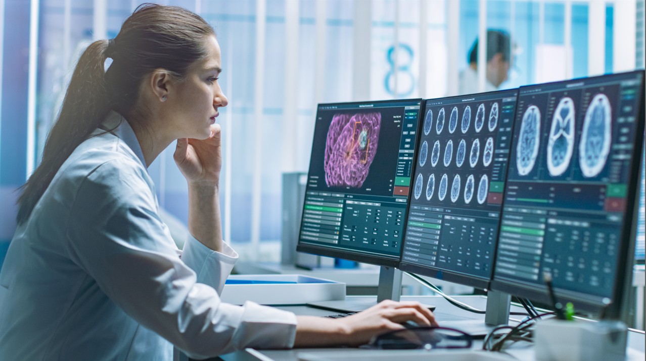 Científica en un laboratorio observando pantallas con imágenes cerebrales y datos complejos, ilustrando la aplicación de las ciencias humanas en el análisis de la salud, la cognición y el comportamiento.