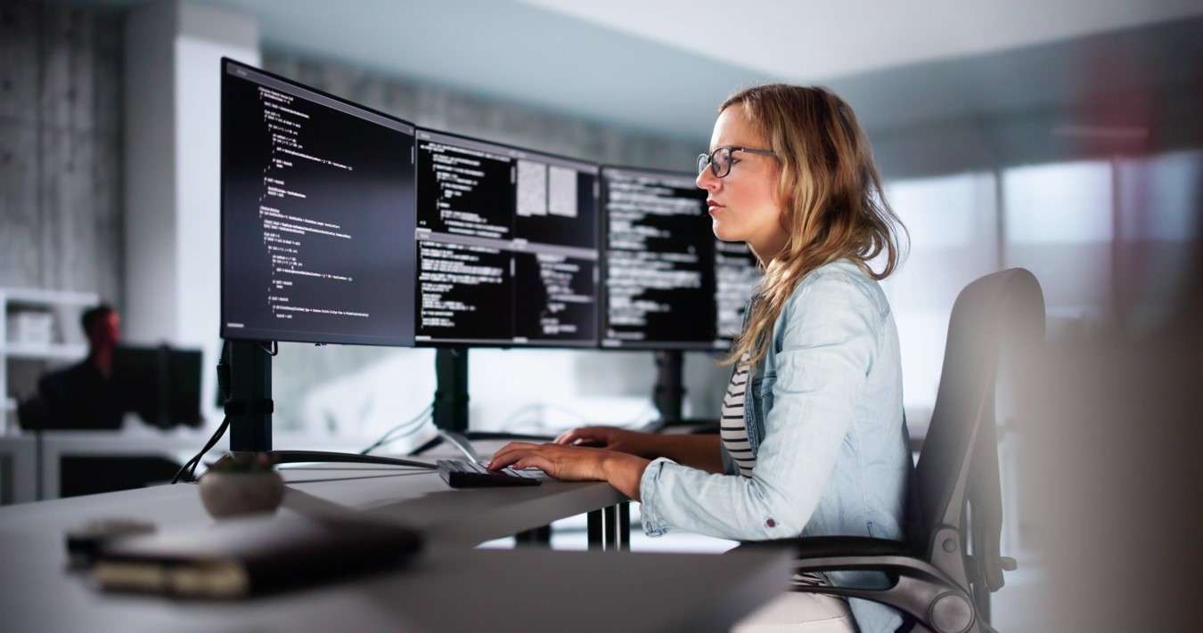 Mujer programando código en múltiples pantallas, reflejando el trabajo de una ingeniera de software o desarrolladora.