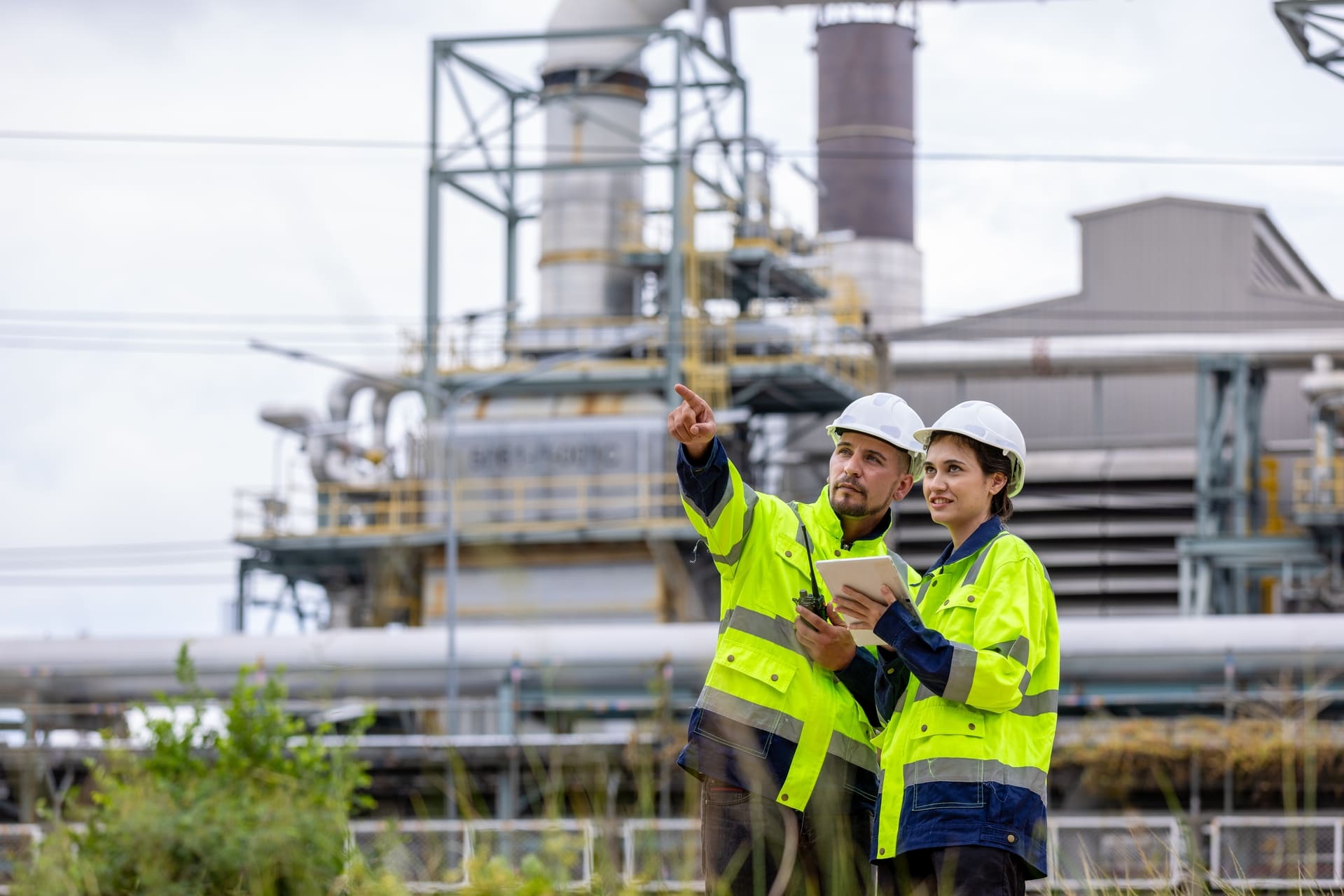 Dos profesionales de ingeniería analizando datos en una planta industrial, ideal para los estudiantes del programa de ingeniería virtual.