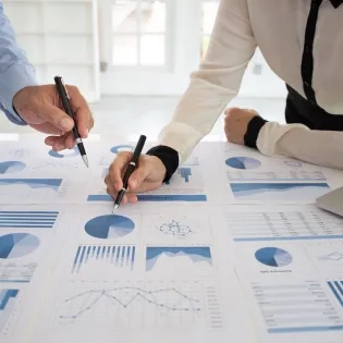 Contadores revisando y comparando gráficos financieros y reportes contables sobre una mesa durante un análisis profesional.