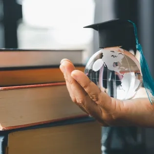 Mano sosteniendo un globo terráqueo con birrete simbolizando el impacto global del postgrado en educación y la mejora del salario docente en el escalafón nacional.