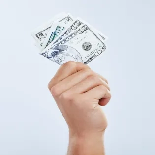 Mano sosteniendo un fajo de dólares, representando el pago de la prima de servicios en el programa de contaduría pública.