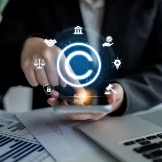 Mano interactuando con iconos legales digitales y de copyright sobre un teléfono, representando la regulación estatal y la propiedad intelectual, temas centrales para entender qué es el Derecho Administrativo. Incluye balanza de justicia y mazo.