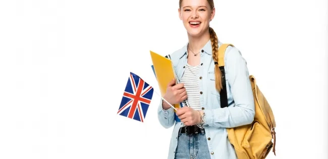 Estudiante feliz con una mochila y carpetas, sosteniendo una bandera del Reino Unido, simbolizando el aprendizaje de lenguas extranjeras y la inmersión cultural.