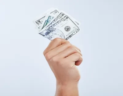 Mano sosteniendo un fajo de dólares, representando el pago de la prima de servicios en el programa de contaduría pública.