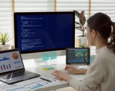 Vista trasera de una estudiante de MBA en su escritorio, rodeada de análisis de datos y gráficos empresariales, representando las competencias clave qué aprenderás en un MBA."