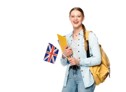 Estudiante feliz con una mochila y carpetas, sosteniendo una bandera del Reino Unido, simbolizando el aprendizaje de lenguas extranjeras y la inmersión cultural.