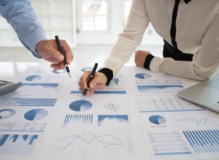 Contadores revisando y comparando gráficos financieros y reportes contables sobre una mesa durante un análisis profesional.