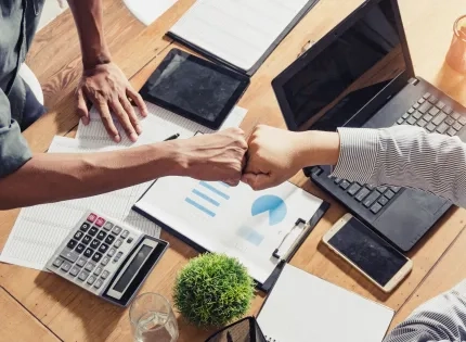 os profesionales celebran con un choque de puños el éxito en la eficiencia empresarial mediante el análisis de datos, enfoque de la Ingeniería Industrial Ibero.