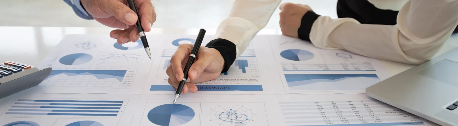 Contadores revisando y comparando gráficos financieros y reportes contables sobre una mesa durante un análisis profesional.