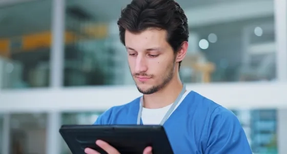 Profesional de la salud utilizando una tablet, representando la implementación de la telesalud y la telemedicina para la atención remota y el acceso a la información del paciente.