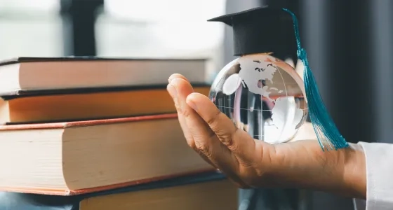 Mano sosteniendo un globo terráqueo con birrete simbolizando el impacto global del postgrado en educación y la mejora del salario docente en el escalafón nacional.