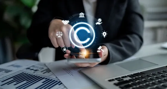 Mano interactuando con iconos legales digitales y de copyright sobre un teléfono, representando la regulación estatal y la propiedad intelectual, temas centrales para entender qué es el Derecho Administrativo. Incluye balanza de justicia y mazo.